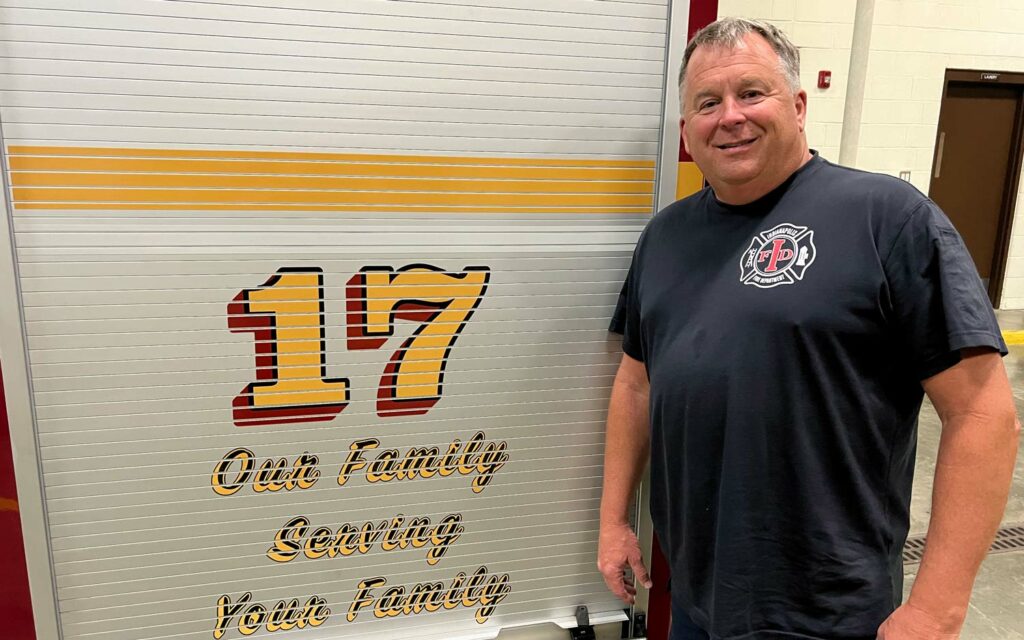 IFD Engine 17 Engineer Dave Yeoman standing next to a wall that has painted "17 Our Family Serving Your Family"